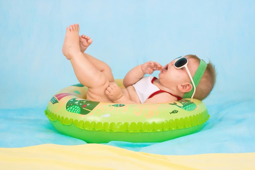 Baby in oversized sunglasses and a green float ring on a blue and yellow summer blanket